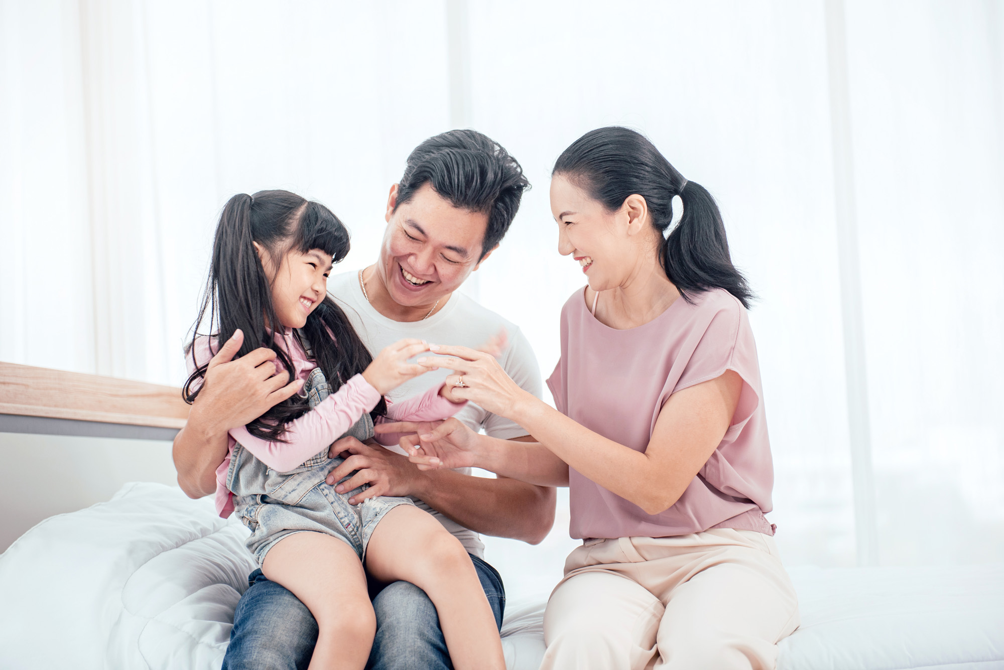 Happy Asian family (mother, father, child daughter) playing together on bed while smile in bedroom at home.